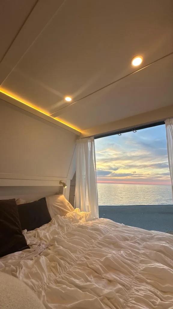 Heckbett im ausgebauten Citroën Jumper mit Blick durchs Seitenfenster aufs Meer im Abendlicht