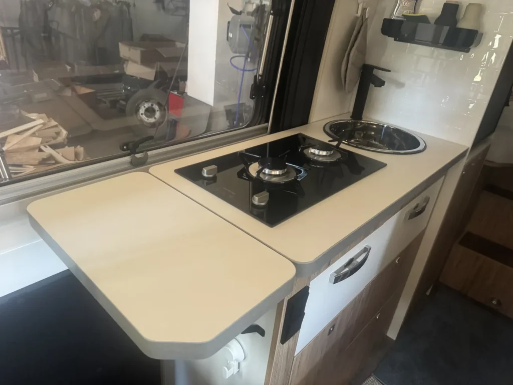 Umgebaute Küche im Pilote 640 mit aufgeklappter Arbeitsplatten-Verlängerung, Glas-Gaskochfeld und separatem Waschbecken