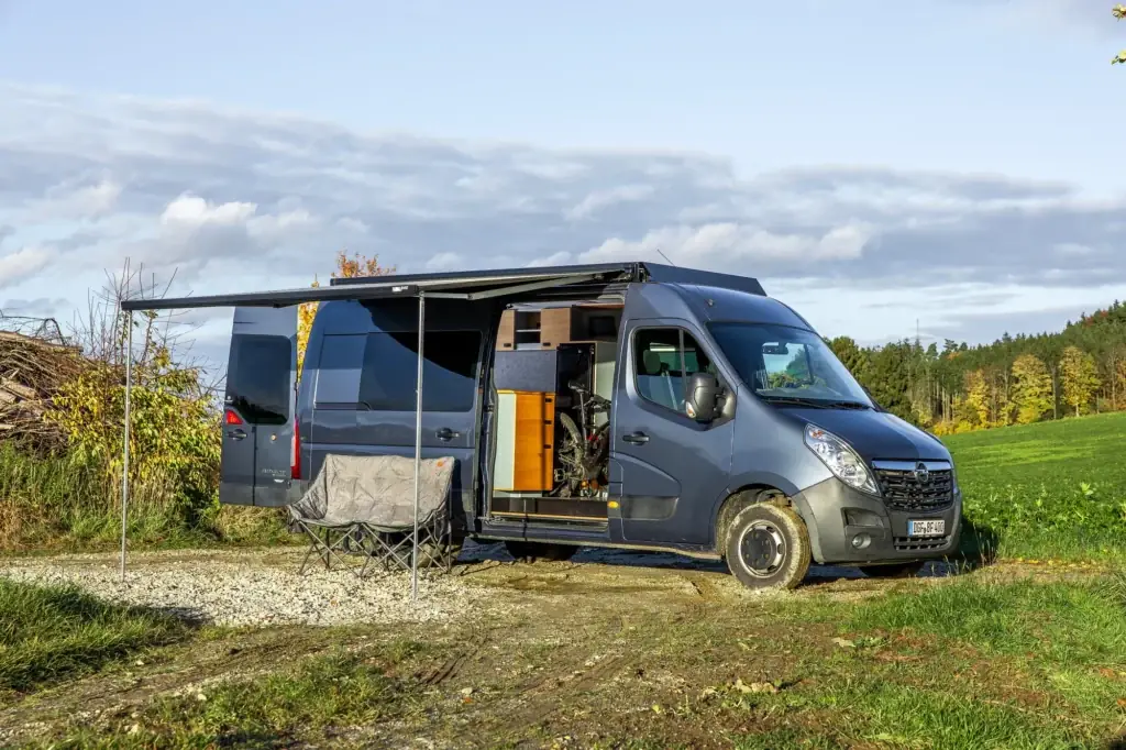 Movano mit ausgefahrener Markise, Campingstühlen und Blick in den Innenraum